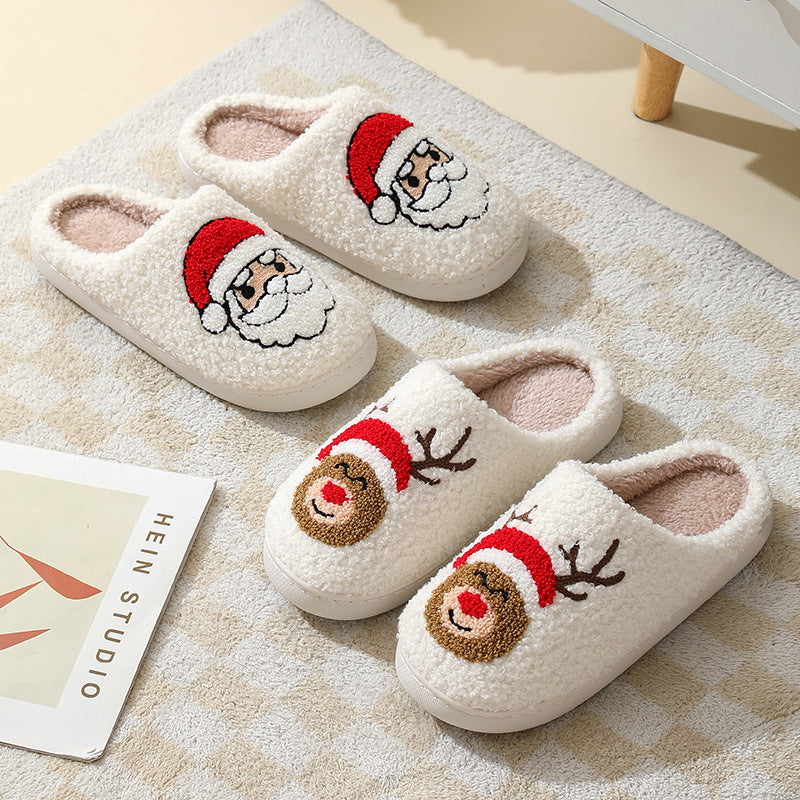 Pair of white slippers with Santa and reindeer faces on a textured surface.