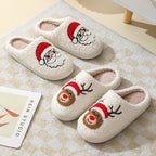 Pair of white slippers with Santa and reindeer faces on a textured surface.