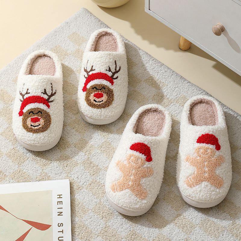 Pair of white slippers with reindeer and gingerbread man designs on a textured surface.